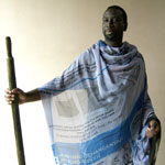 A black man stands in blue printed fabric