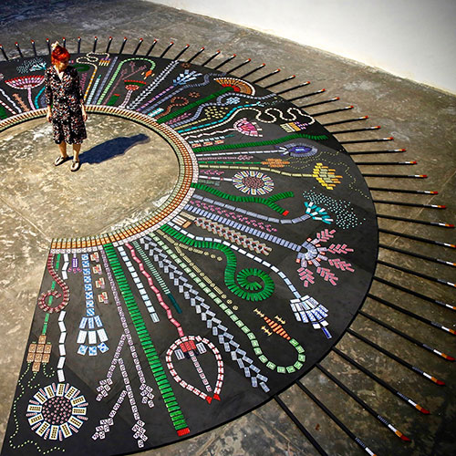 The artist Susie Freeman standing in the middle of a large circular piece with pills in the shapes of plants and flowers