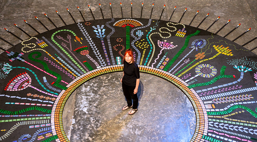 The artist Susie Freeman standing in the middle of a large circular piece with pills in the shapes of plants and flowers